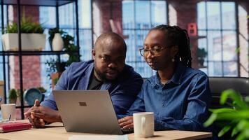 African american life partners working remotely in cozy loft, planning development strategies and discussing project ideas while using laptop to track progress. Camera B. photo