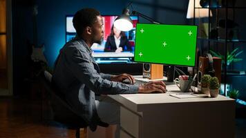 Male freelancer sitting at desk with copy space screen on computer, browsing web and enjoys remote work. Young man multitasking and networking, relaxing at home. Camera A. photo