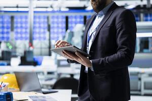 Quality control analyst in a solar manufacturing plant evaluates workflow, dressed in suit to reflect corporate oversight and business leadership. Technical knowledge in sustainable energy. photo