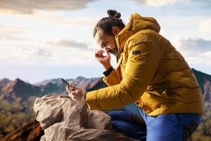 Young trekker being distracted by his phone on top of the mountain, dealing with technology addiction and always connected to the internet. Explorer enjoying scenic landscape view. photo