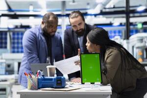 Solar panel diverse group reviewing insight on pc next to green screen, finding errors during a process audit and helping optimize renewable energy operations. Photovoltaics factory. photo