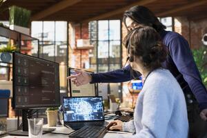 Call center manager guiding intern on how to use AI chatbot at office desk on PC. Asian customer support workplace onboarding specialist teaching woman to use artificial intelligence software photo