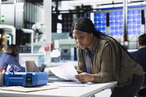 Woman master engineer reviewing production line data on papers, manages factory activity in a solar panel plant to ensure effective quality control and commitment to renewable energy tech. photo