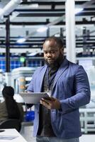 African american business person walks through modern factory inspecting solar panel machinery, reading important insight for the corporate commitment to sustainability and renewable power. photo