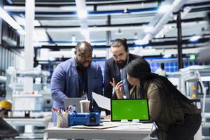Multiethnic energy specialists coordinates activity next to chroma key, taking quality control measures in a solar tech facility. Corporate oversight and industrial execution. photo