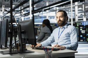 Data center programmer using PC to update servers tech, configuring gear using software tools. Server farm worker reviewing hardware analytics, ensuring reliable network operations photo