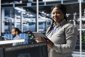 Portrait of smiling data center programmer using tablet to update servers tech, configuring gear using software tools. Happy server farm worker reviewing hardware analytics using device photo
