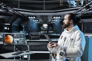 Cosmonaut in orbital station using tablet to verify navigation coordinates towards Mars. Man working on orbital station analyzing mission logs and doing Martian surface research photo
