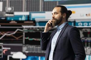 Professional businessman answering a phone call surrounded by KPI metrics to evaluate company performance and insight. Using remote communication to improve his business, greatness. photo