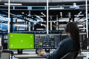 Programmer in data center using isolated screen computer to check equipment performance upgrading infrastructure. IT expert doing maintenance on supercomputers in servers room using chroma key PC photo