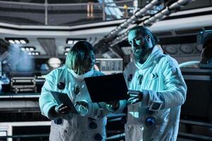 Teamworking astronauts doing brainstorming to confirm suit integrity using laptop. Orbital station colleagues talking, testing gear during routine equipment check using notebook photo