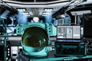 Close up of space helmet next to laptop running ship systems interface inside futuristic spacecraft. Notebook dashboard readouts metrics and astronauts equipment prepared for flight photo
