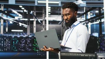 Data center programmer uses node tree software to identify equipment performance issues. African american server farm worker reviews data analysis graph to minimize hardware failures, camera B photo
