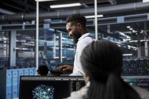Data center system administrator uses AI visualization tech to oversee automated repetitive tasks. African american man in server farm modifying infrastructure rigs based on data analytics graphs photo