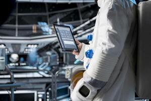 Close up of astronaut using tablet to view spacecraft analytics during scientific mission. Spaceship crew member in spacesuit looking at orbital navigation data on device during planetary exploration photo