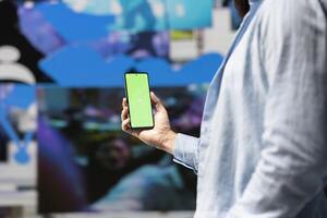 Male influencer holds phone with chroma key screen for online presence, using his imagination and storytelling skills to connect with followers and boost online engagement. Modern web design. photo
