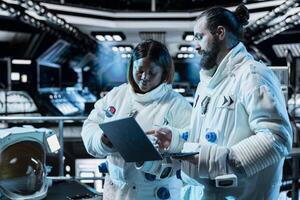 Team of cosmonauts running telemetry software on laptop, preparing for planetary mission outside. Astronauts checking thrusters diagnostics using notebook, beginning landing procedures on planet photo