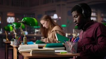 Black guy using music to help with deep focus for academic success, consulting campus university database to find reliable sources. Male college student fights for diploma. Camera A. photo