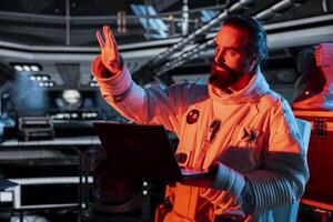 Spaceship crew member stressed by unknown hull breach causing alarm to sound. Worried cosmonaut reacts to system failure as radiation spike triggers emergency red lights inside orbital cockpit photo