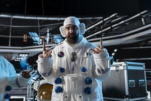 Smiling astronaut doing playful hand gestures inside space station during relaxation moment with crew. Joyous quirky cosmonaut enjoying himself with humor inside futuristic starship photo