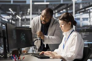 Data center manager supervising worker using artificial intelligence neural networks tech. Server farm team leader overseeing engineer using AI programming language on computer to update equipment photo