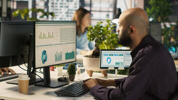 Employee editing documents on computer at office desk, updating reports and files. Worker analyzing data charts on desktop screen, interpreting statistical information, camera A photo