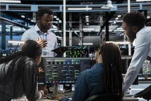 Engineers doing brainstorming, programming in server farm housing infrastructure storing datasets. Teamworking colleagues run code on PC to repair data center racks doing computational operations photo