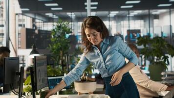 Upset worker in office packing desk plants on last day at work after quitting, saying goodbye to colleague. Employee getting fired from job during layoffs, camera A photo