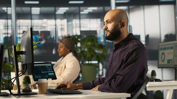 Arab man reviewing financial graphs, analyzing key performance indicators. Middle Eastern employee in workspace looking over data trends and strategic insights, camera A photo