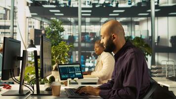 Accountant in busy workplace talking with colleagues while inputting financial figures on PC. Employee working in modern office chatting with coworkers and crosschecking data, camera B photo