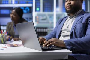 African american solar panels plant executive troubleshooting technical issues using notebook. Photovoltaics factory manager analyzing data using laptop, reviewing system health metrics, close up photo