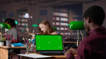 Young student working with a green screen in the university campus library, collecting academic information from verified educational sources. Pupil using research tools. Camera A. photo