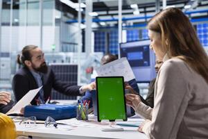 Investors review documentation on mockup device to evaluate investment profitability. Shareholders and production plant manager analyzing sustainable manufacturing data using isolated screen tablet photo
