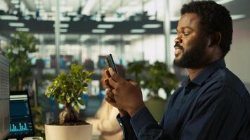Employee taking break from checking documents to text friends using smartphone, relaxing. Accountant in office pausing tasks to answer messages on mobile phone, camera B photo