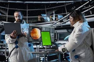 Orbital station coworkers analyzing Mars planetary data using green screen tablet. Team of astronauts in spaceship doing red planet surface research using chroma key device photo
