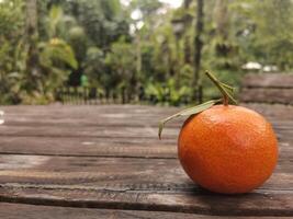 A single mandarin orange with leaf on a wooden table with green nature background. Copy space. Agricultural products. From the farm to the table. Vegetable food. photo