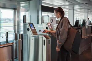 A young woman uses her smartphone to scan a boarding pass at an automated airport gate. Concept of digitalization, self-check-in and independent travel. photo