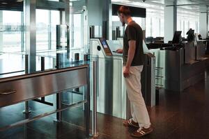 A young man uses her smartphone to scan a boarding pass at an automated airport gate. Concept of digitalization, self-check-in and independent travel. photo