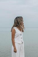 unrecognizable woman with wavy hair in a white outfit stands by a still lake, gazing to the side. the image conveys a serene and contemplative mood, emphasizing inner peace and self connection. photo