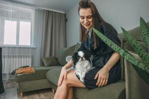 woman in black robe on green couch with dog gazing and looking at camera on her lap in softly lit cozy living room, pet care, wellness, lifestyle blog photo