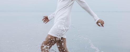woman in white dress splashing through shallow water in motion, only body and arms, dynamic composition with serene lake background, concept of lifestyle, wellness, clothing brand photo