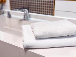 Soft white towels neatly stacked on a clean countertop in a modern bathroom setting. photo
