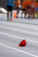 Red sports cap lying on the ground of a running track with blurred athletes in the background photo