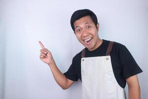 Excited face expression young asian man wearing apron pointing right side, empty space. photo