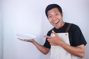 Happy face expression asian man chef or waiter shows empty white plate, presenting something photo