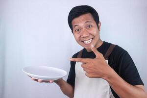 Excited face expression asian man chef or waiter shows empty white plate, presenting something photo
