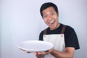 Funny expression asian man chef or waiter shows empty white plate, presenting something photo