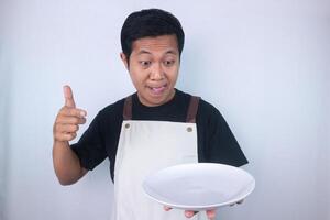Funny expression asian young man look at delicious dish while stuck out his tongue, want to eat it photo