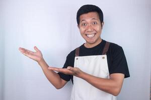 Smiling face expression young asian man wearing apron pointing right side, empty space. photo