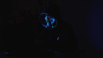 Cyber terrorist in hoodie on laptop working in shadows to represent hacking activity and online danger video
